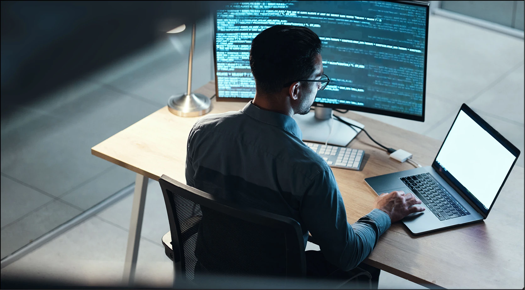 Developer optimizing production network performance by coding at a desk with multiple monitors.
