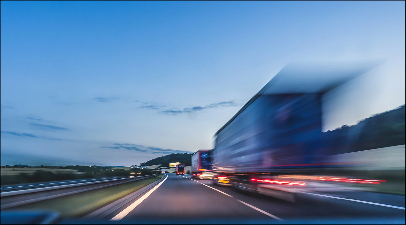 Blurred trucks on highway at dusk, illustrating supply chain logistics
