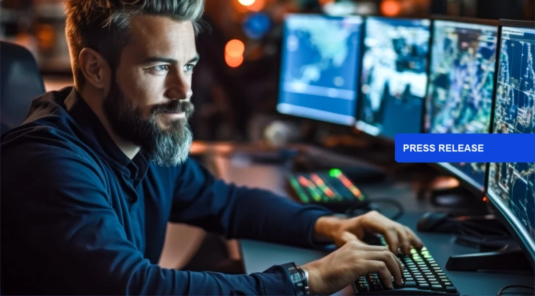 Man with beard working on computers with "Press Release" overlay