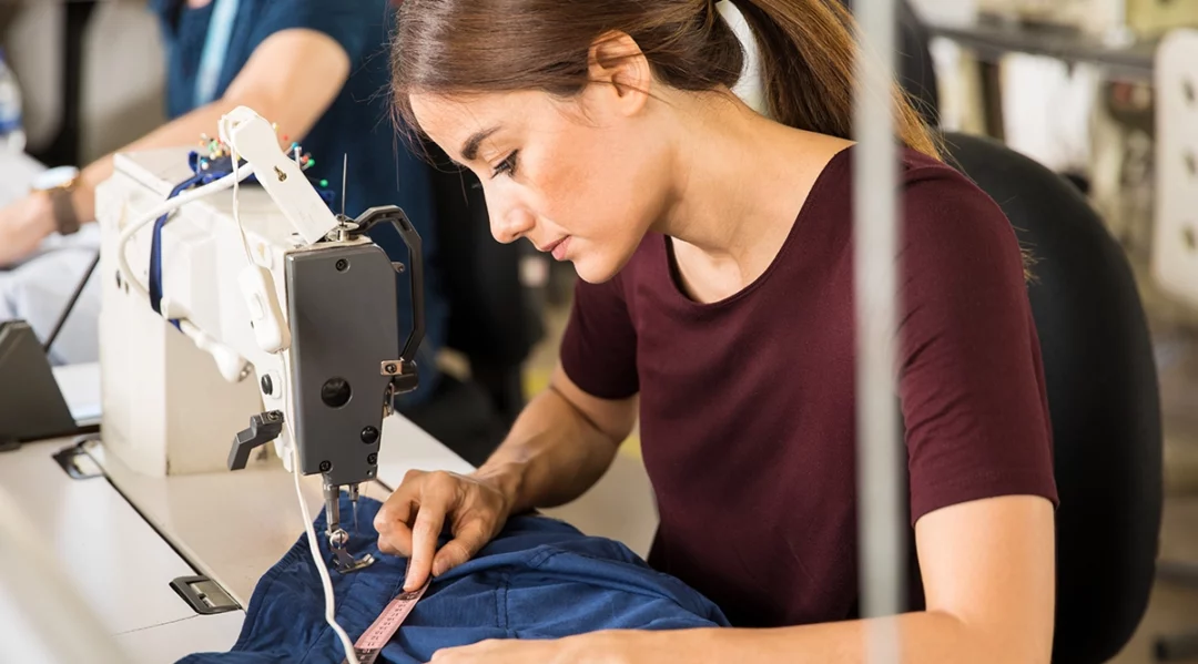 Seamstress measuring fabric on a sewing machine, symbolizing garment industry production.