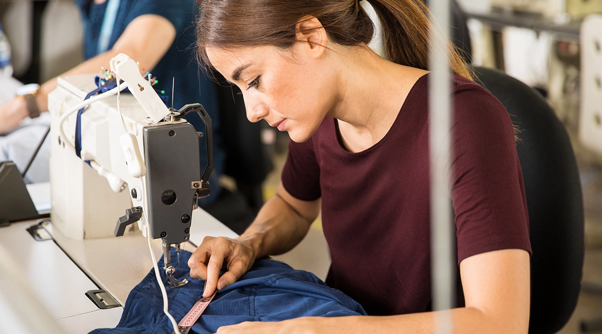 Seamstress measuring fabric on a sewing machine, symbolizing garment industry production.