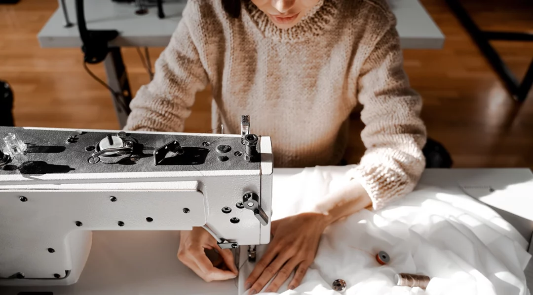 Woman sewing white fabric on a sewing machine, luxury apparel compliance