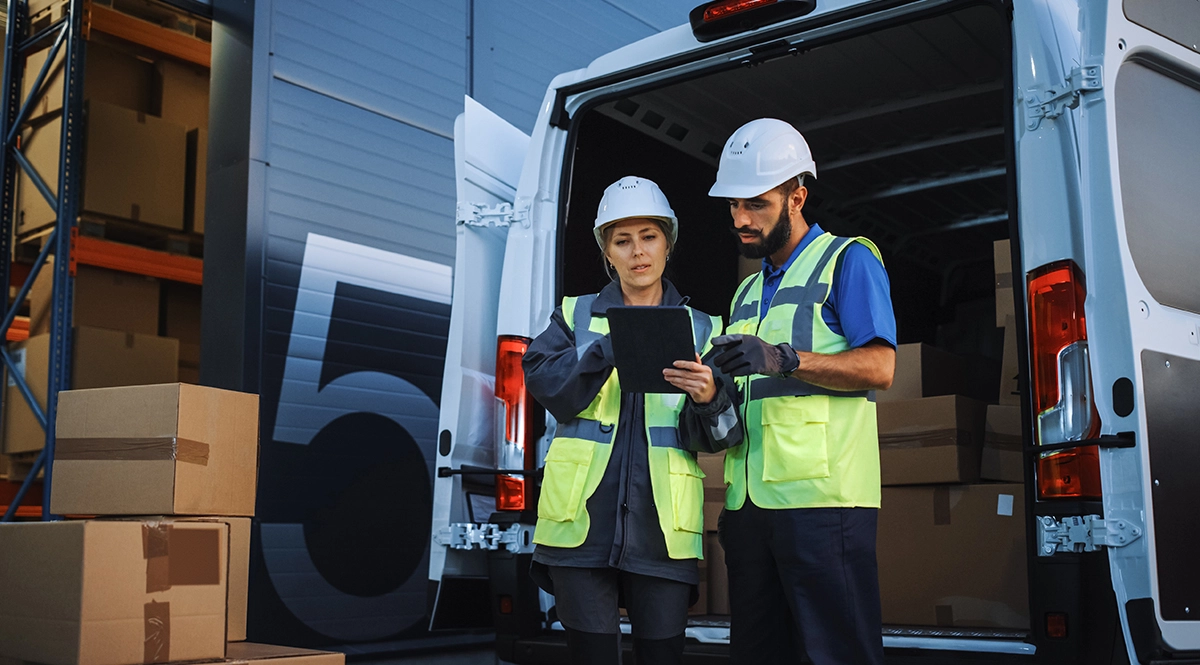 Warehouse workers check digital product passport data on a tablet near a delivery van.