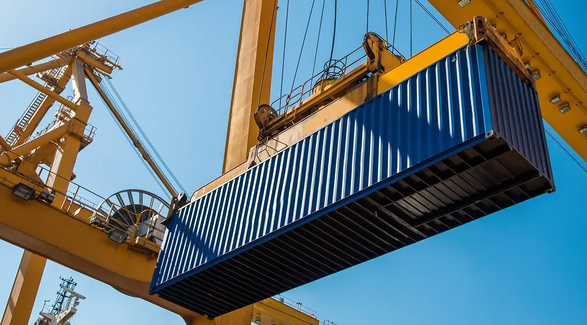 Yellow crane lifting a blue shipping container, symbolizing global trade shifts.