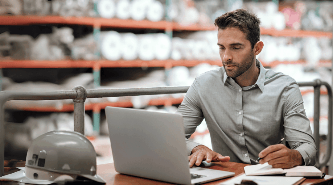 Man in warehouse using laptop for supply chain risk management.