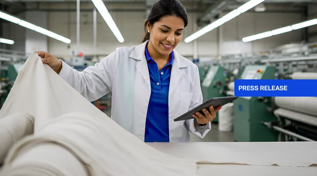 Woman in lab coat inspects fabric in factory, with "PRESS RELEASE" overlay.