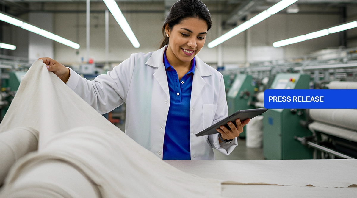 Woman in lab coat inspects fabric in factory, with "PRESS RELEASE" overlay.
