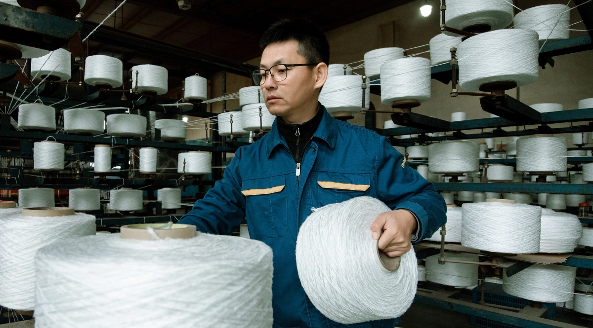 Man in factory holding large spool of white yarn, textile production