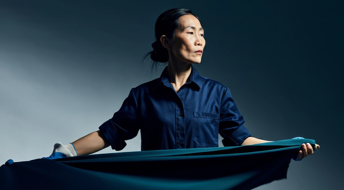 Woman in blue shirt and gloves holds dark fabric, highlighting traceability.