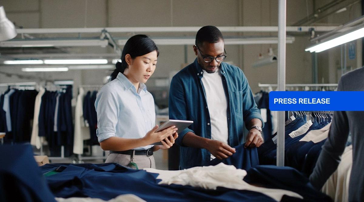 Two people in a garment factory review fabric, with "PRESS RELEASE" overlay.