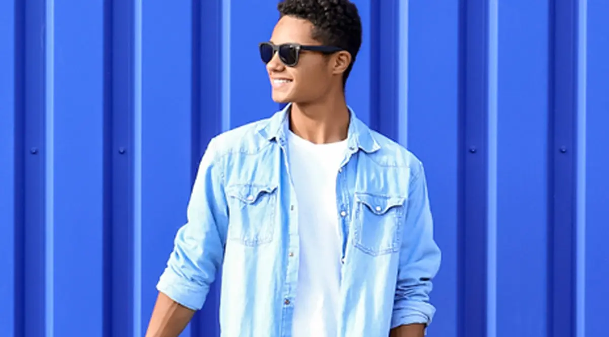 Young man in sunglasses and denim shirt against blue background